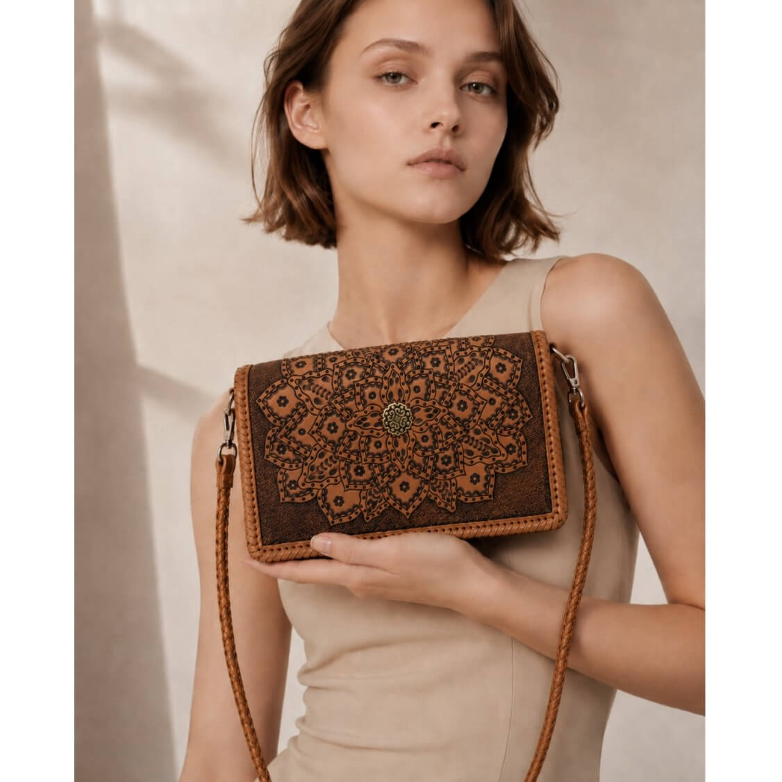 Woman holding a brown leather handbag with intricate patterns against a neutral background