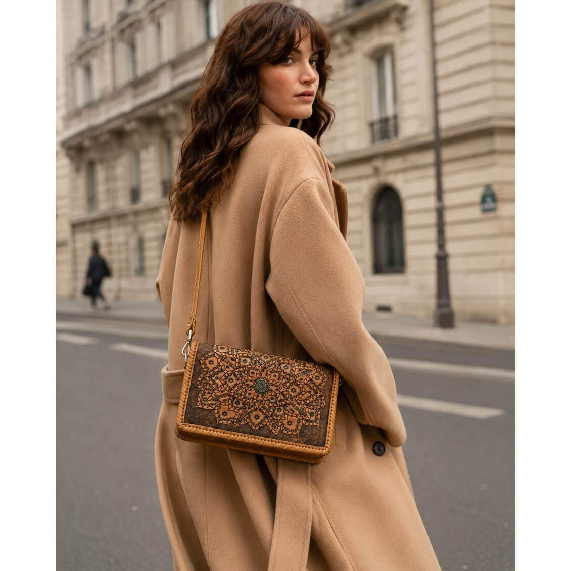 Woman in a beige coat with a full grain leather patterned handbag walking on a city street.