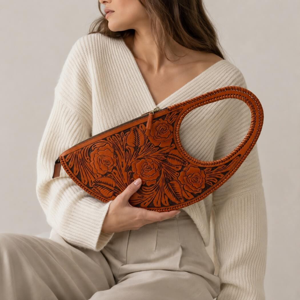 Model holding a burnt orange hand-tooled leather handbag with floral rose detailing and braided top handle.