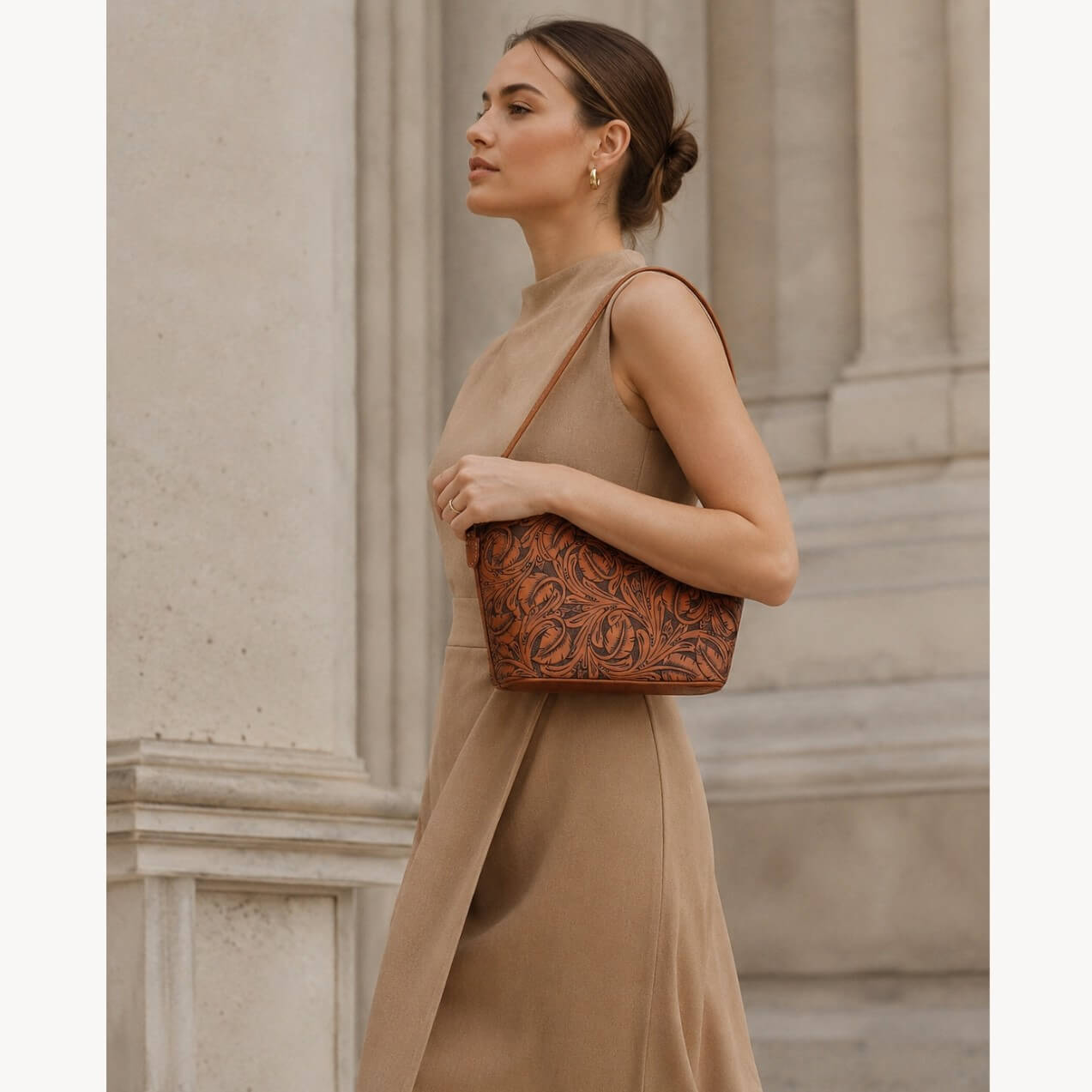 Model wearing a burnt orange hand-tooled leather shoulder bag with floral detailing and a slim shoulder strap.