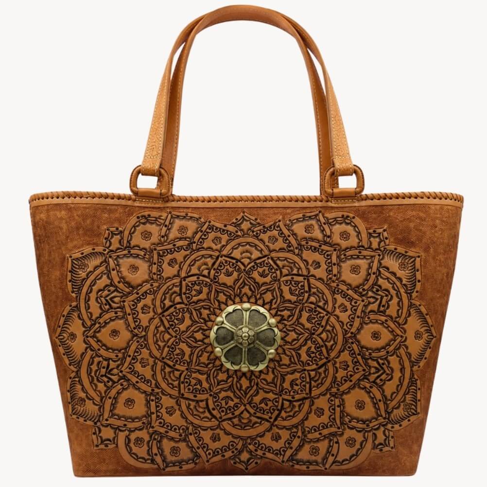 Cognac/burnished brown nude color tooled leather tote with floral medallion hardware and double shoulder straps on a white background.