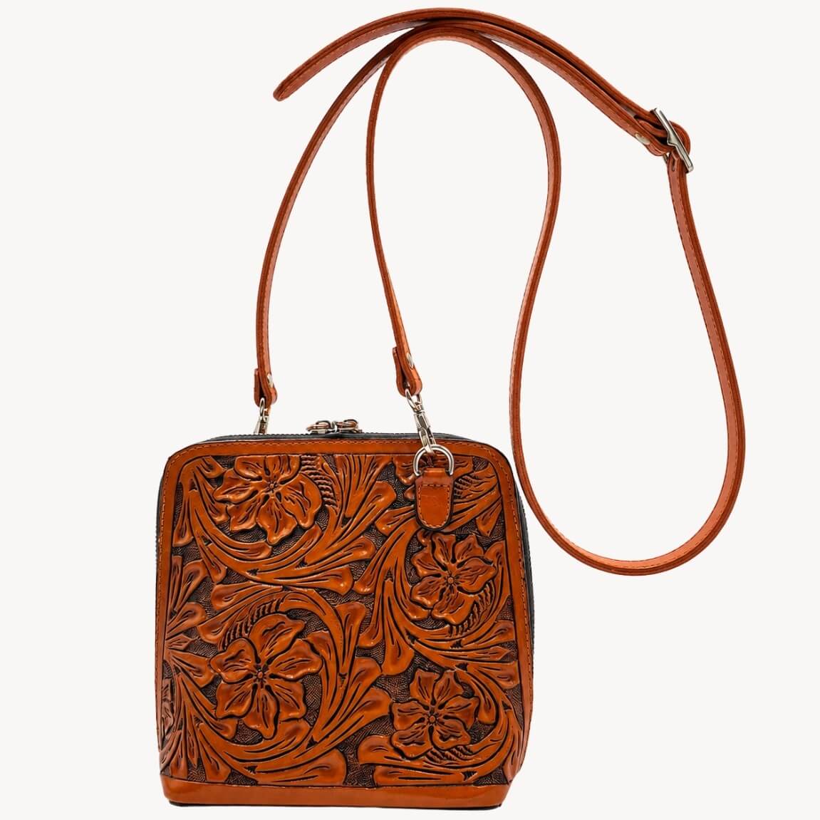 Burnt orange hand-tooled leather crossbody bag with floral design, long adjustable strap, and silver-tone hardware on a white background.