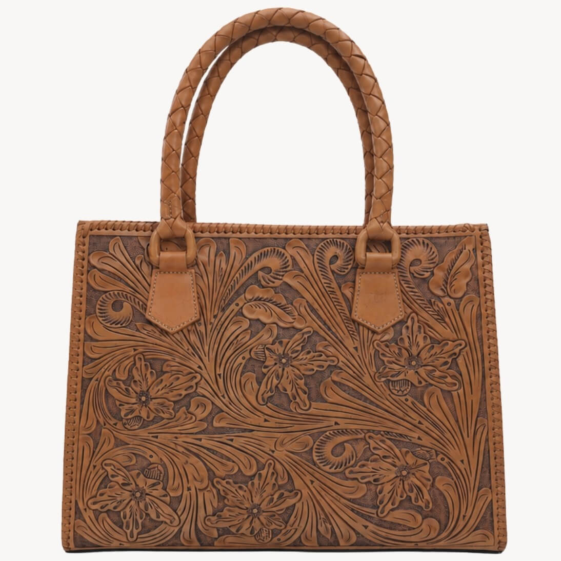 Natural tan hand-tooled floral leather tote bag with braided handles and carved floral detailing on a white background.