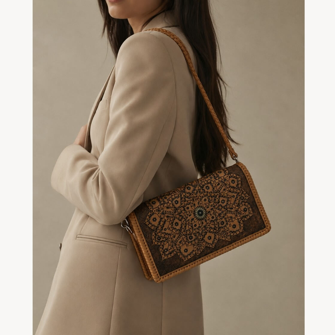Model in a beige blazer wearing a natural tan embossed leather shoulder bag with mandala detailing, braided strap, silver hardware, and circular clasp.