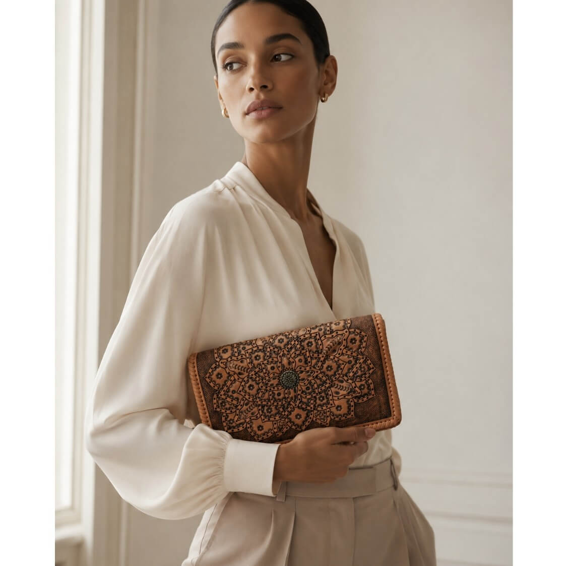 Woman holding a full grain leather clutch with floral pattern in a neutral setting