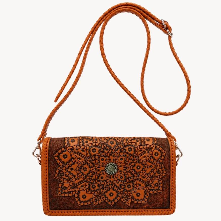 Burnt orange embossed leather crossbody bag with mandala detailing, braided shoulder strap, silver hardware, and circular metal clasp on a white background.