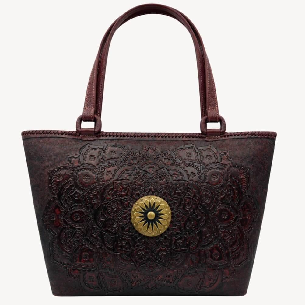 Mahogany espresso embossed leather tote handbag with top handles, ornate tooled pattern, and round gold medallion.