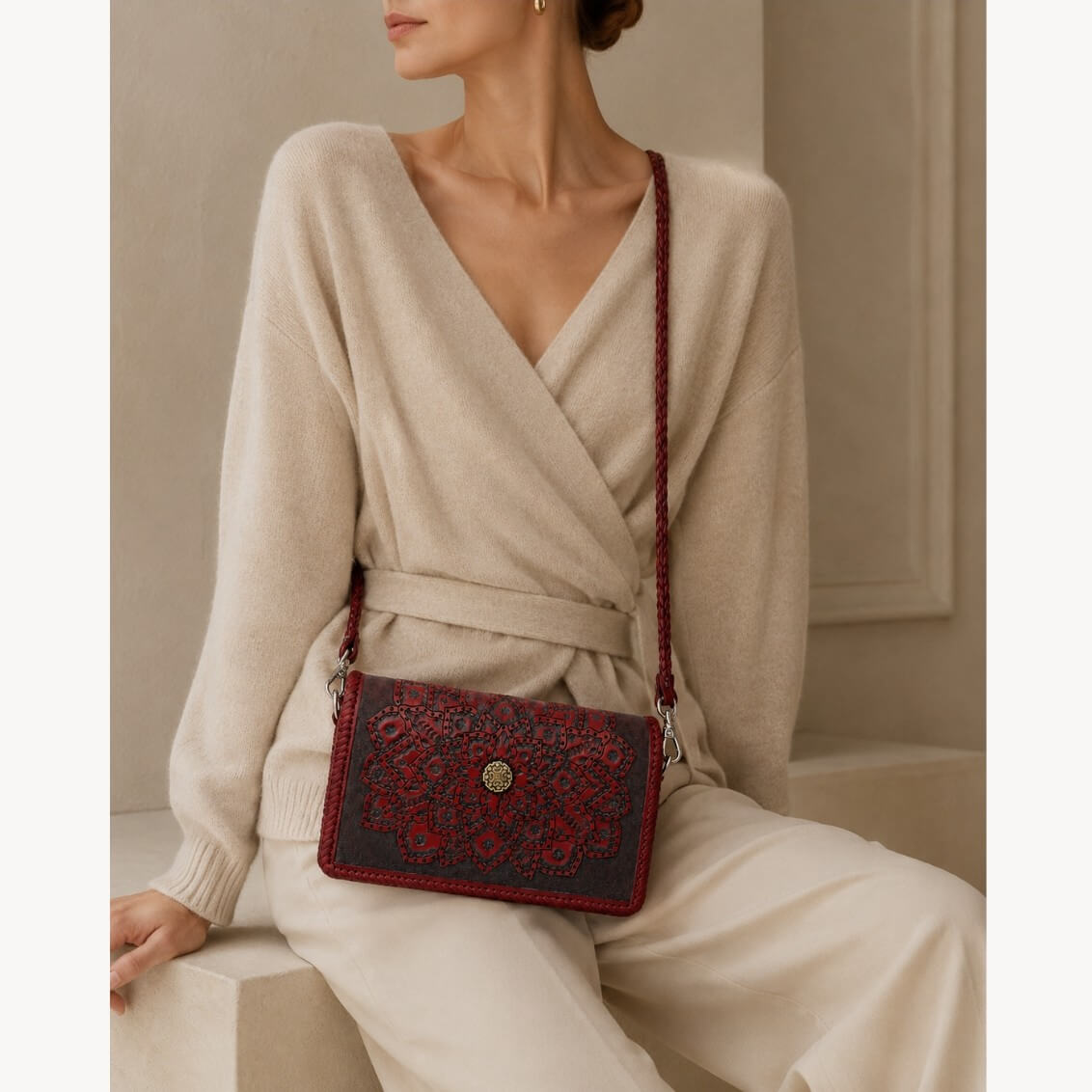 Model in a cream wrap sweater wearing a Mahogany Espresso embossed leather crossbody bag with mandala detailing, braided strap, silver hardware, and gold circular clasp.
