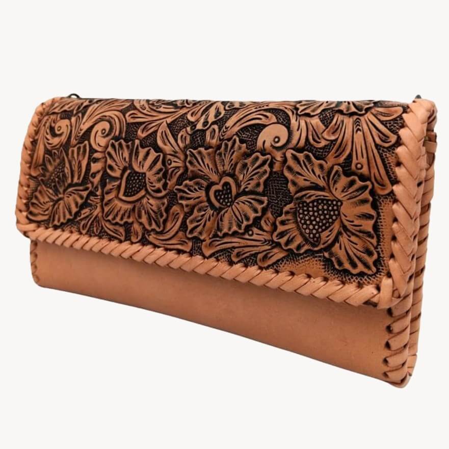 Angled left view showing floral/leaf tooling and braided edge on full grain leather clutch.