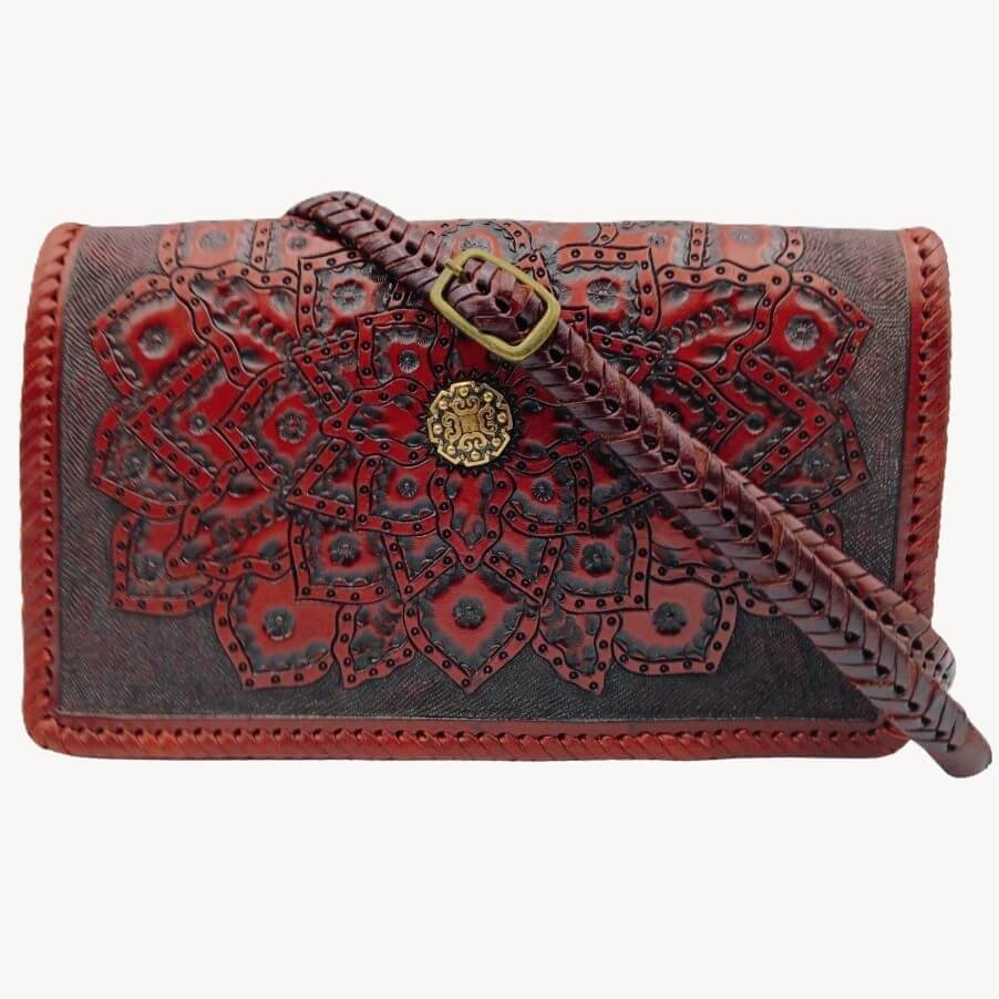 Crossbody strap attached—hand‑braided look with brass buckle on tooled mandala flap.