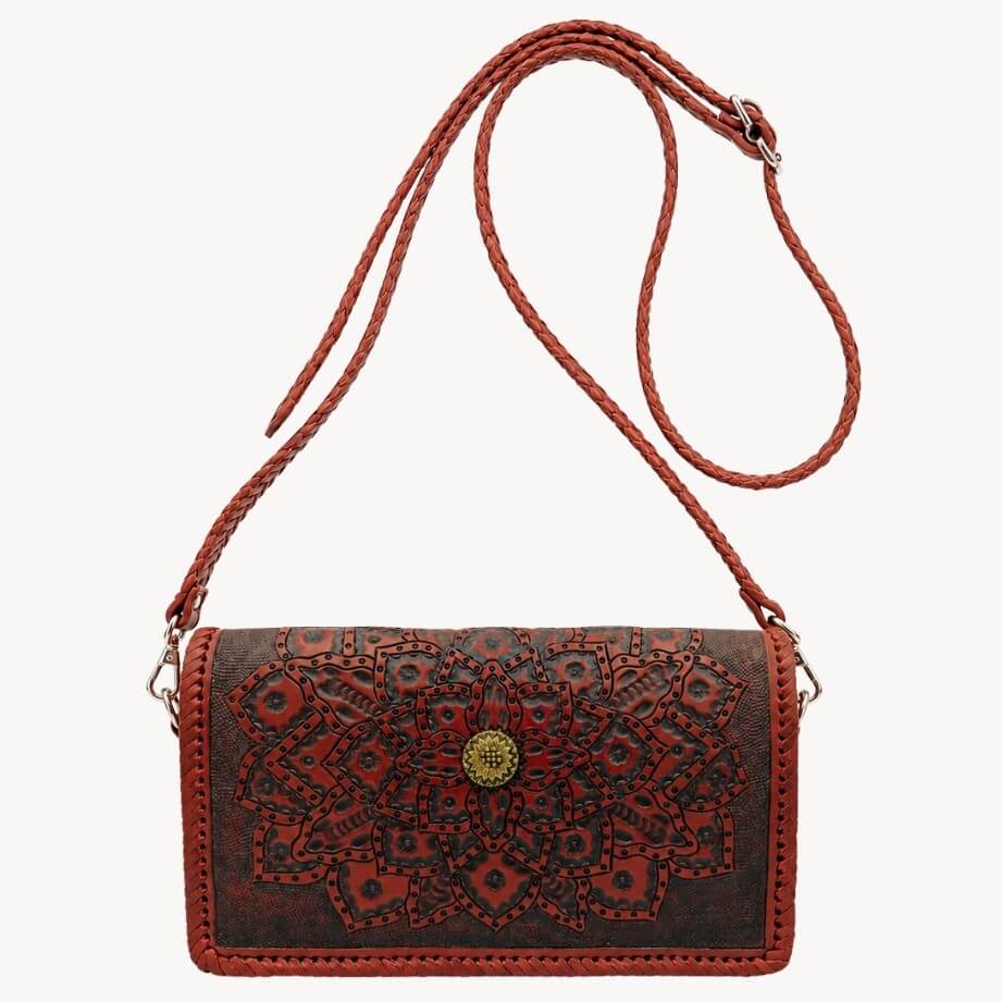 Red-brown embossed leather crossbody bag with mandala detailing, braided shoulder strap, silver hardware, and a gold circular clasp on a white background.